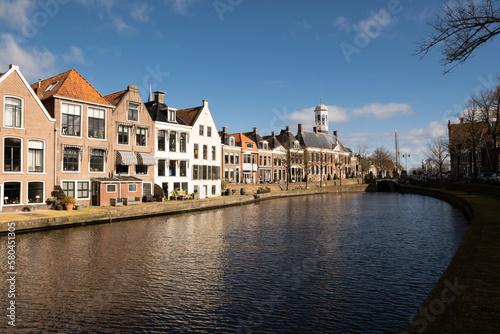 waterside residential houses on the edge of the river kleindiep waterway in Dokkum, Friesland, Netherlands Holland. old town hall in town centre with bridge on pleasant sunny day