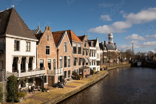 waterside residential houses on the edge of the river kleindiep waterway in Dokkum  Friesland  Netherlands Holland. old town hall  in town centre with bridge on pleasant sunny day