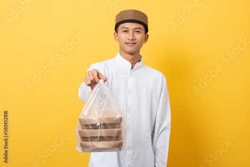 Young handsome asian muslim man giving alms or charity standing over orange background. happy ramadan and eid al-fitr. photo
