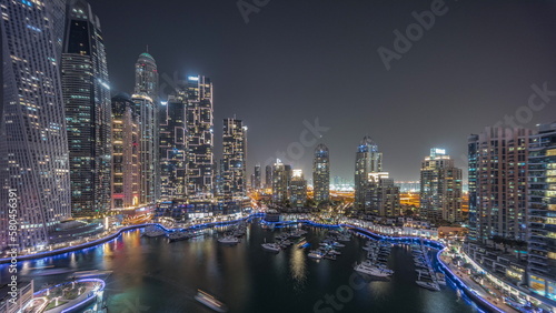 Dubai marina tallest skyscrapers and yachts in harbor aerial night timelapse.