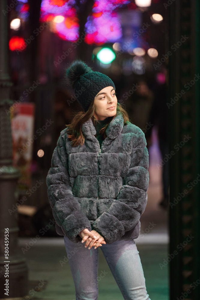 Woman in winter clothes looking in a window of a night store . Winter season concept.