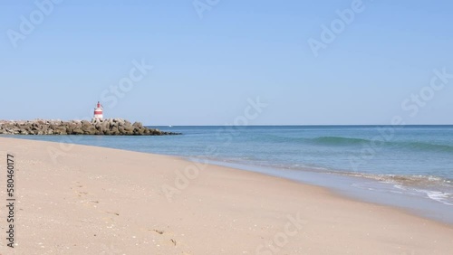 Video of beach and lighthouse on jetty on Tavira Island, known as Ilha de Tavira in the Algarve in Portugal. 4K video with ocean sound