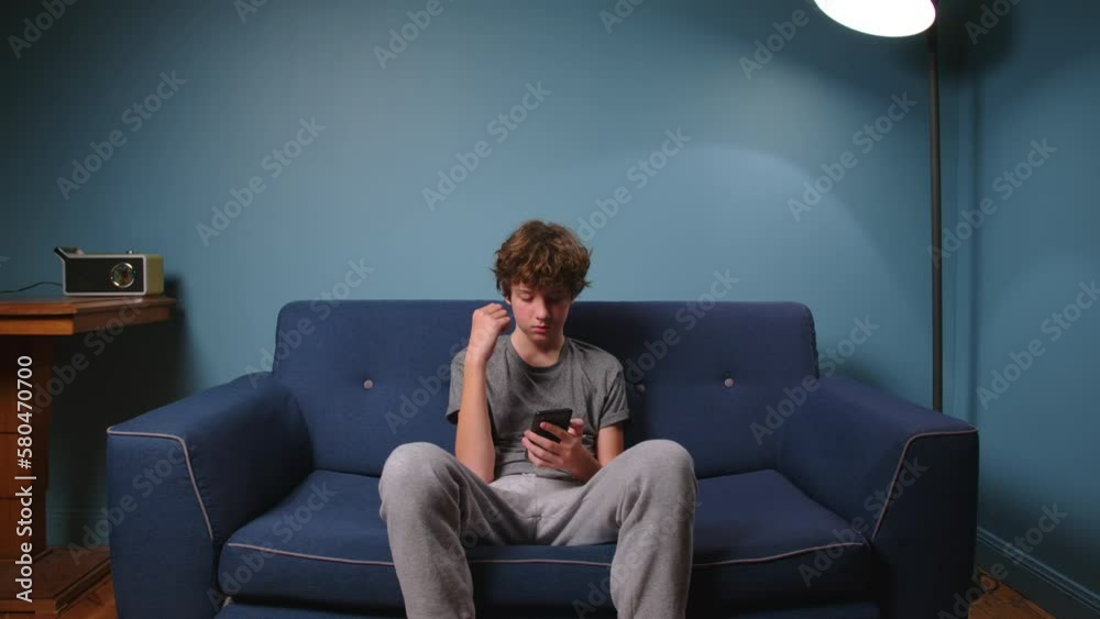 Teenager sits on the couch without talking. Boy addicted to gadgets, using mobile phone, laptop at home. Internet obsession concept Teenager sits on the couch without talking. Boy addicted to gadgets, using mobile phone, laptop at home. Internet obsession concept