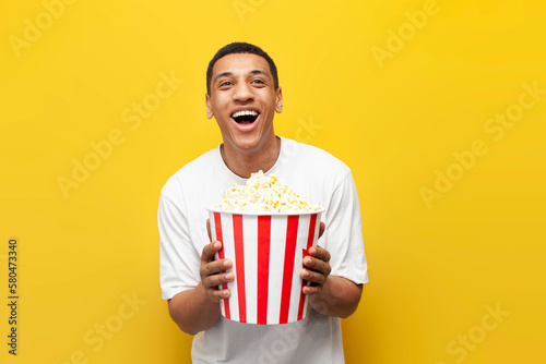 Photography young african american guy with popcorn watching comedy and laughing on yellow i