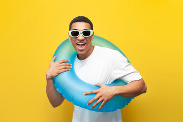 cheerful young guy afro american in sunglasses with inflatable swimming ring on yellow isolated background