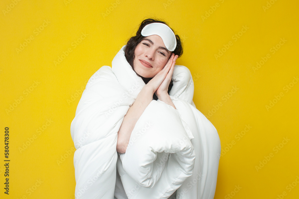 cute young girl in sleep mask and with warm soft comfortable blanket stands on yellow background cute young girl in sleep mask and with warm soft comfortable blanket stands on yellow background