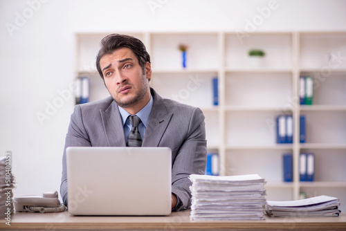 Young male employee and too much work at workplace