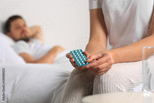 Couple in bedroom. Woman with blister of oral contraception pills, closeup
