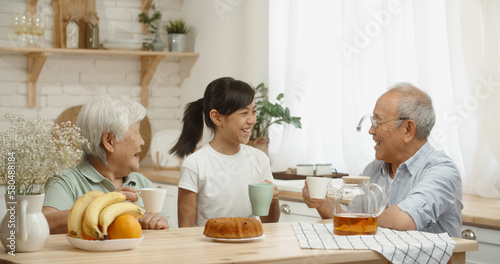 Asian pensioneer couple spending time with their granddaughter, drinking black tea, chatting and relaxing - family bonds, relationship concept  photo