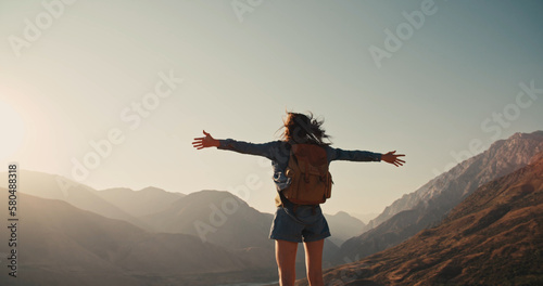 Young girl standing on top of mountain and victoriously raising hands up, looking far away - zennism, freedom, adventure concept  photo