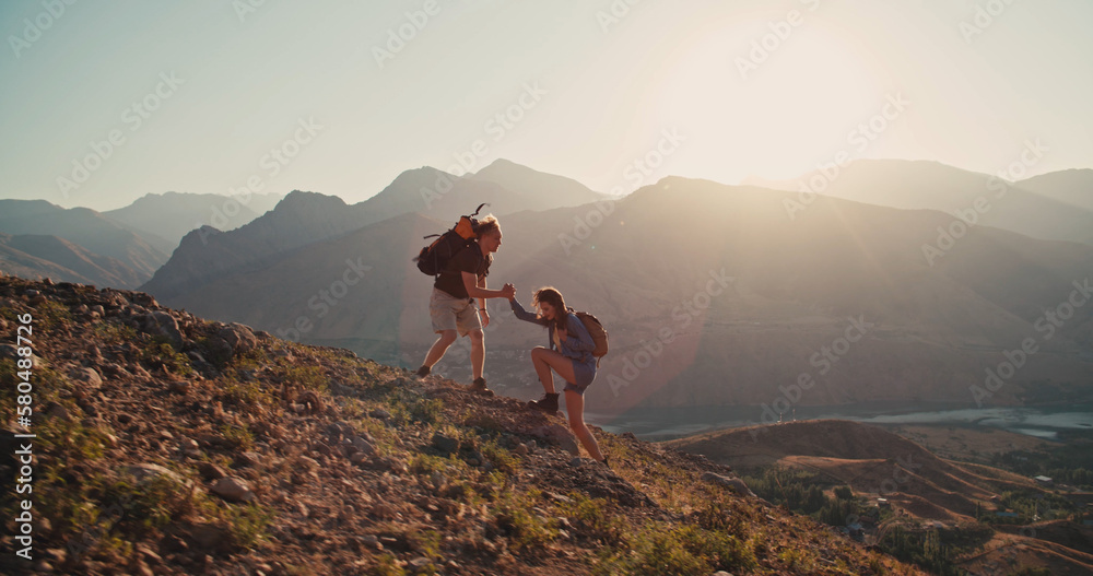 Caucasian girl climbing up a mountain, getting hand of help from her