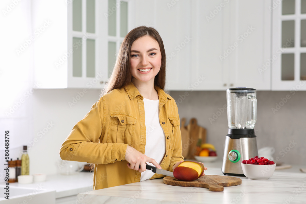 Woman preparing mango for tasty smoothie at white marble table in kitchen