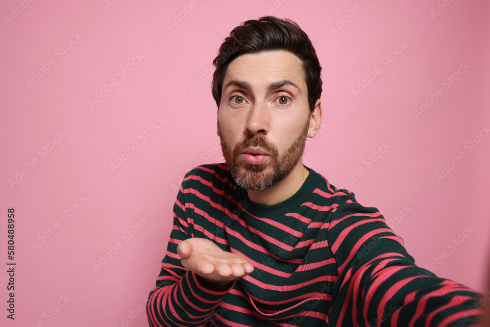 Handsome man blowing kiss while taking selfie on pink background. Space for text Handsome man blowing kiss while taking selfie on pink background. Space for text