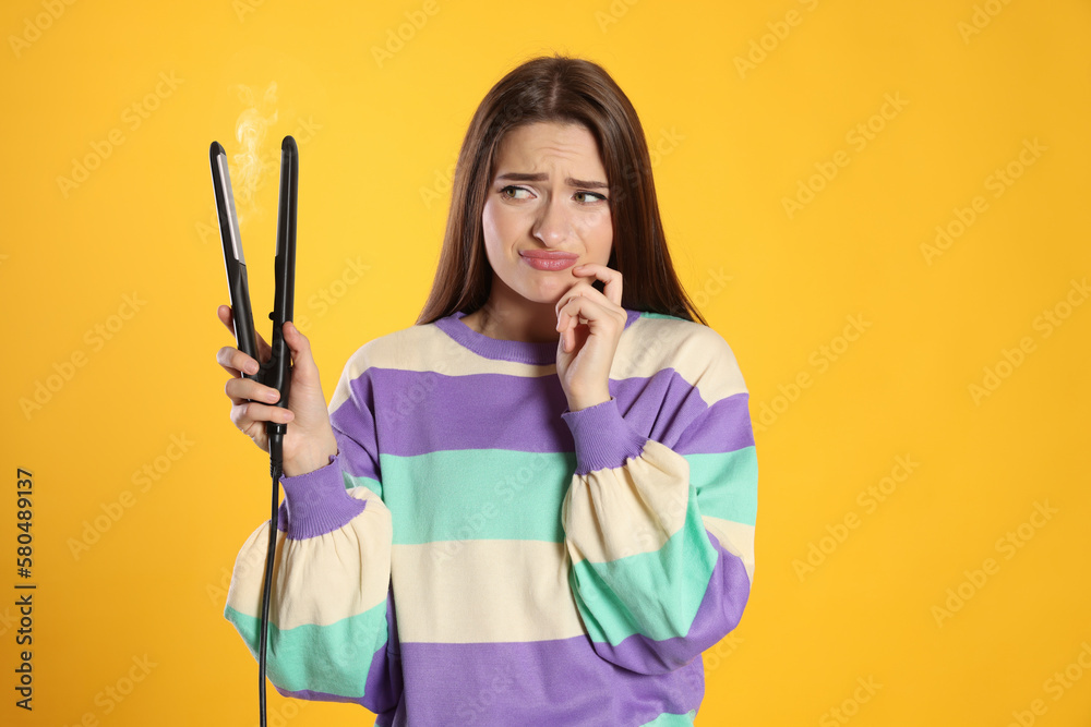 Upset young woman with flattening iron on yellow background. Hair damage Upset young woman with flattening iron on yellow background. Hair damage