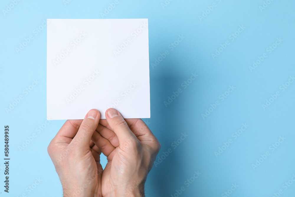 Fototapeta premium Man holding sheet of paper on light blue background, top view. Mockup for design