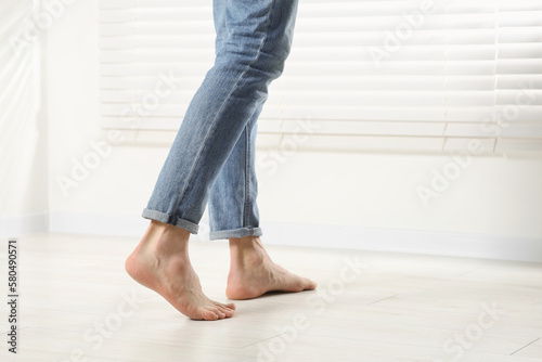 Barefoot man walking on white parquet indoors, closeup. Heated floor