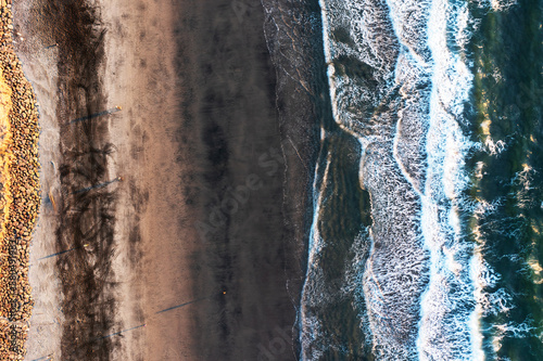 Vertical Aerial Photograph at Rockaway Beach, Oregon with vertical bands of wet and dry beach sand, incoming waves, magnetite on the beach, tracks, erosion control rocks