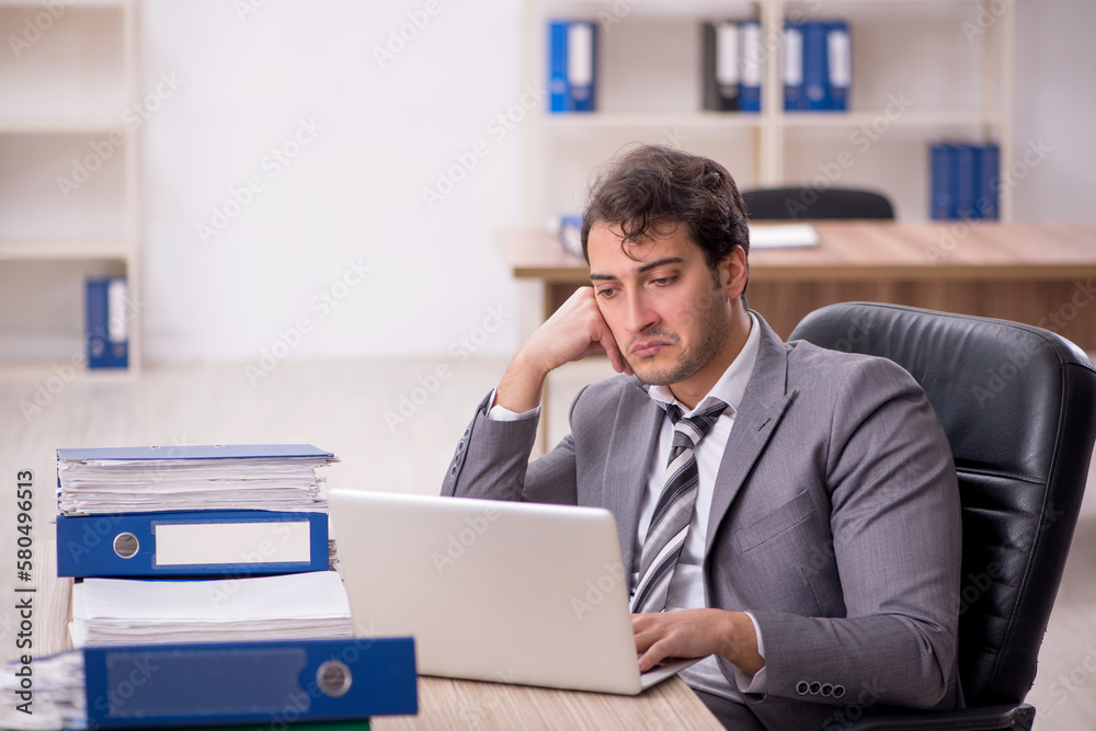 Young male employee unhappy with excessive work in the office Young male employee unhappy with excessive work in the office
