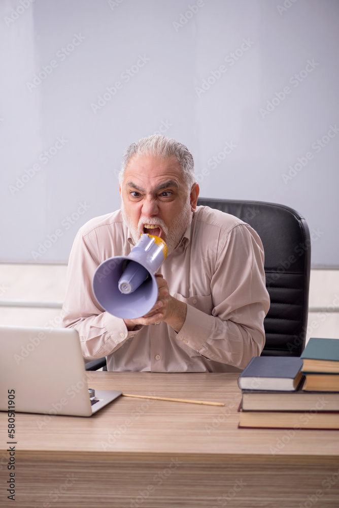 Fototapeta premium Old male teacher holding megaphone in the classroom