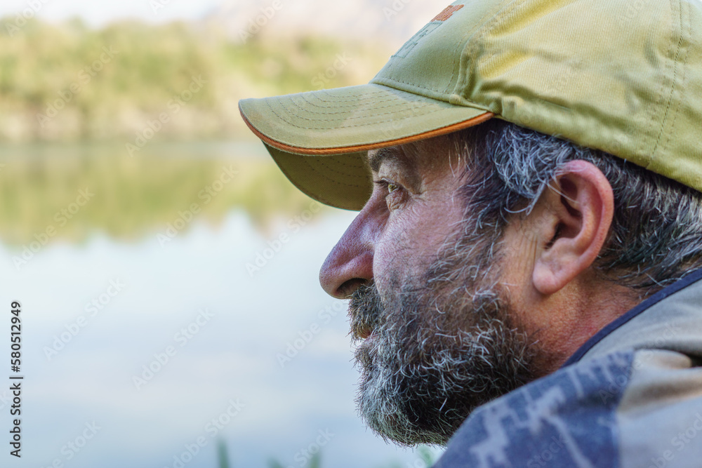 close-up of a fisherman with beard and cap seen in profile on the river bank close-up of a fisherman with beard and cap seen in profile on the river bank