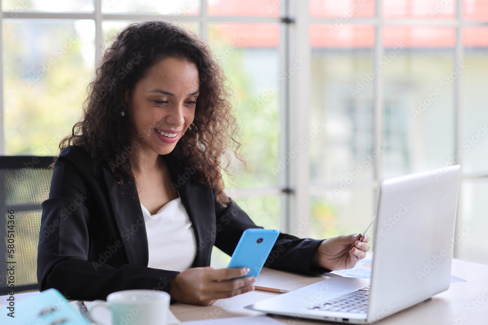 Attractive professional latin female employee worker sitting, using laptop computer with paperwork at home workplace. Businesswoman talking on smart mobile phone and communicate with client. Attractive professional latin female employee worker sitting, using laptop computer with paperwork at home workplace. Businesswoman talking on smart mobile phone and communicate with client.