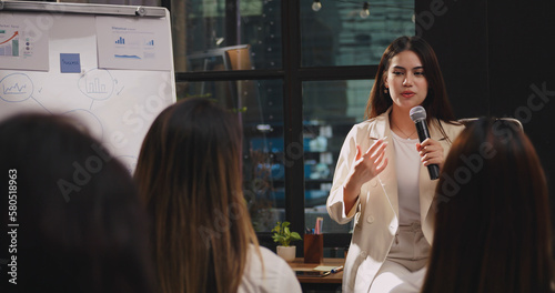 Confident young businesswoman or speaker sharing ideas with colleagues or audience during company seminar.