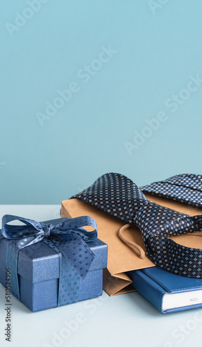 Happy Fathers Day background tall banner. Flat lay Happy Fathers Day gift box and brown paper bag, necktie and agenda on pastel blue table.