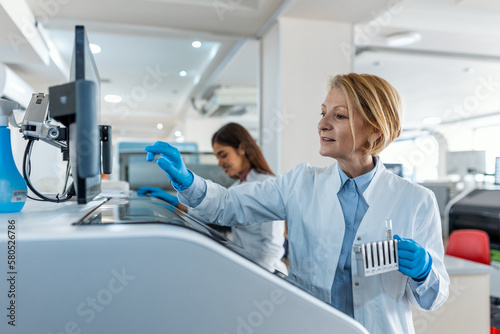 Portrait of a young female laboratory assistant making analysis with test tubes and analyzer machines sitting at the modern laboratory