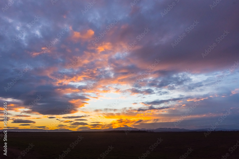 blue and colorful clouds at the sky during sundown n a flat landscape