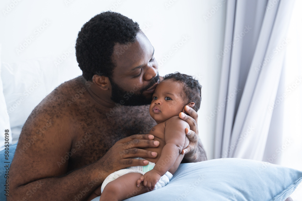 Obraz premium African American bearded father kissing and lull cute newborn baby in his arms and hand at bedroom at home, infant boy 2 months old lying on pillow, African American family and newborn care concept