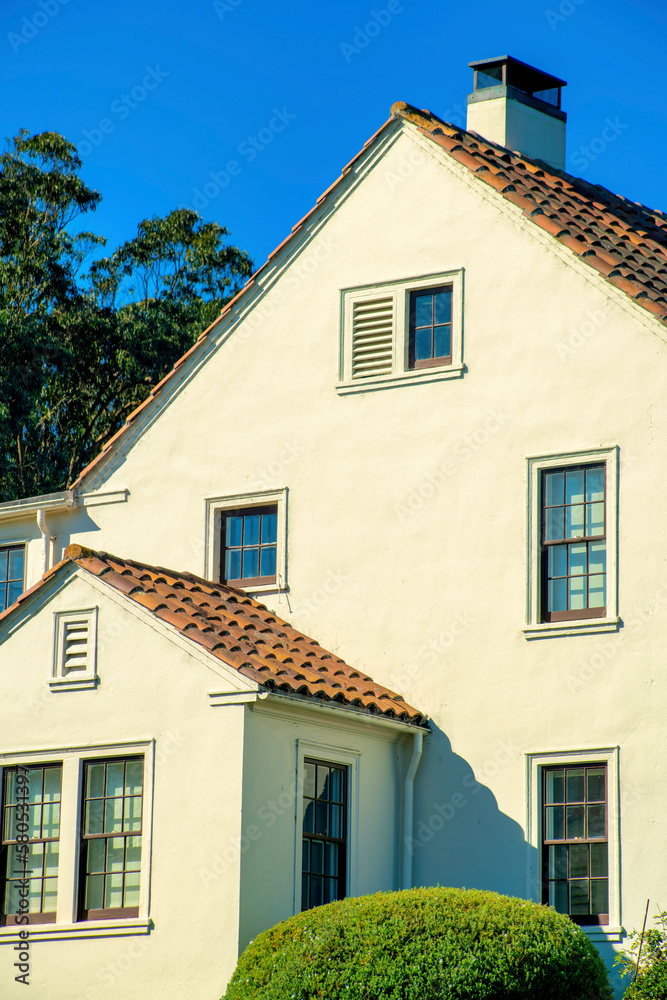 White timber house facade with wooden exterior and gray red roof tiles and visible windows and chimney vents