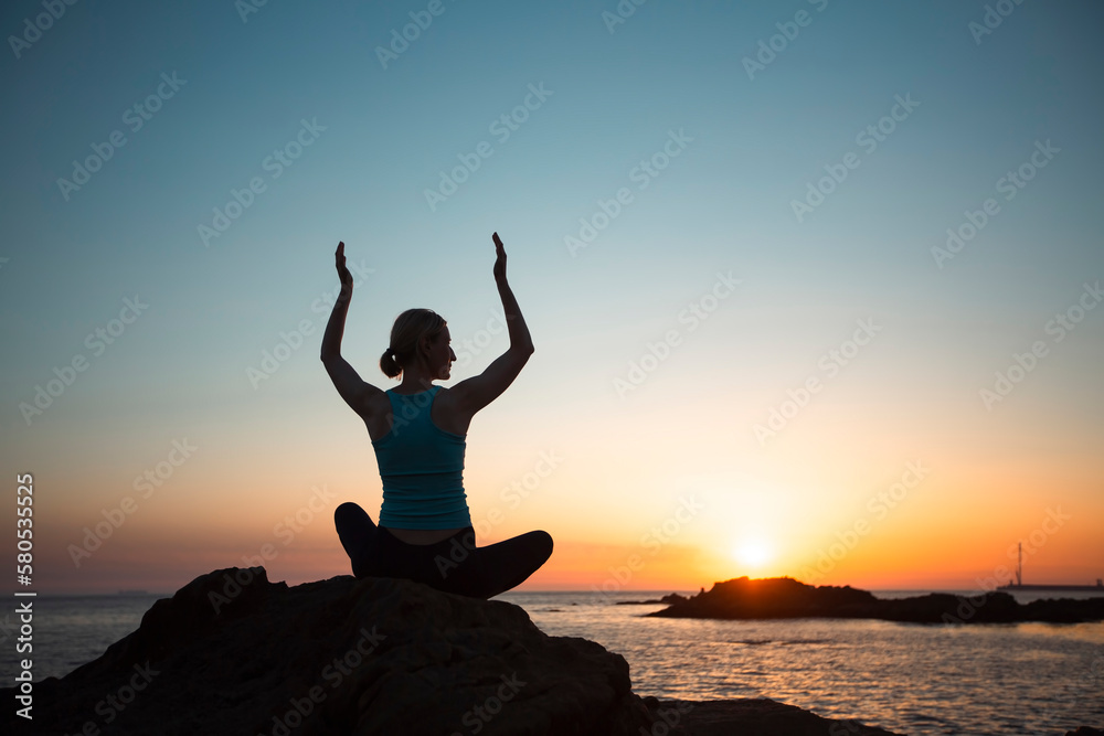 Silhouette of a female yogi on the ocean shore during an amazing sunset.