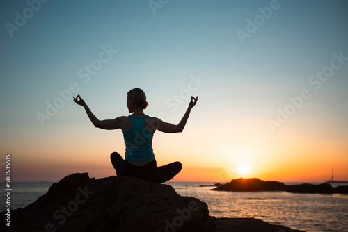 Yoga women silhouette on the ocean shore during an amazing sunset.