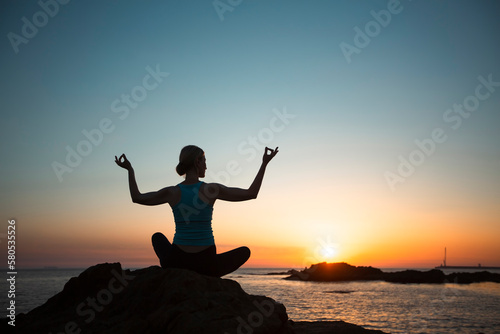 Silhouette of a middle-aged yoga woman on the ocean  during sunset.