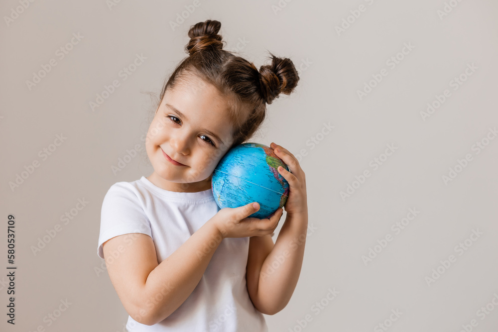a happy little girl is holding a small globe planet in her hands in a white T-shirt on a white background. Earth Day, space for text a happy little girl is holding a small globe planet in her hands in a white T-shirt on a white background. Earth Day, space for text