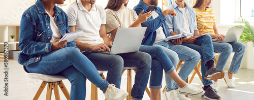 Diverse people in casual clothes using notebooks and laptops during personal development training. Cropped image of multiracial men and women sitting in row on chairs in bright office. Panoramic view.