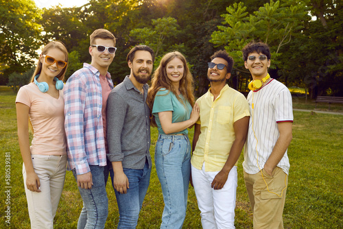 Group portrait of six happy beautiful young people posing in a green summer park. Several cheerful diverse mixed race friends meet in the park and have fun together. Friendship concept