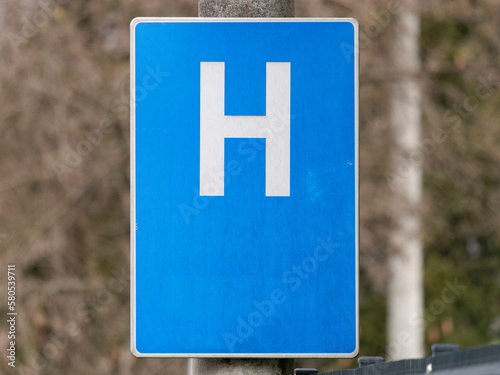 Close-up shot of a Hospital sign on a metal pole with a trees in the background