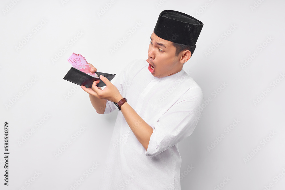 Surprised young Asian Muslim man looking at cash money in wallet isolated on white background. People religious Islamic lifestyle concept Surprised young Asian Muslim man looking at cash money in wallet isolated on white background. People religious Islamic lifestyle concept