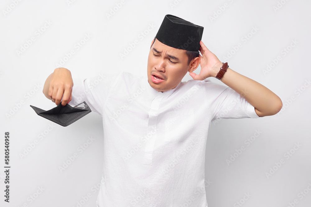 Portrait of unhappy young Asian Muslim man looking empty wallet while touching head isolated on white background. People religious Islamic lifestyle concept