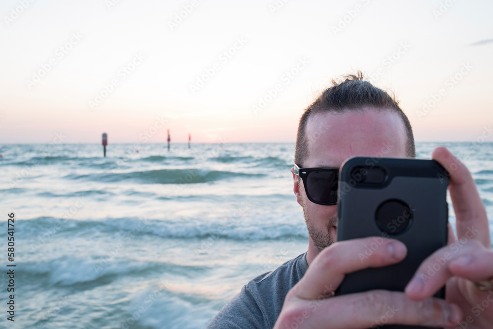 Man photographing through smart phone against seascape during sunset Man photographing through smart phone against seascape during sunset