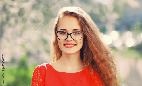 Portrait of happy caucasian smiling young woman in eyeglasses in spring garden on flowers background