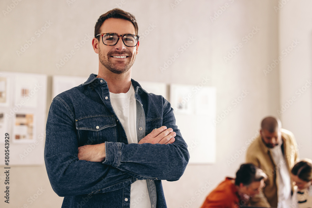 Fototapeta premium Happy young businessman smiling at the camera with his arms crossed
