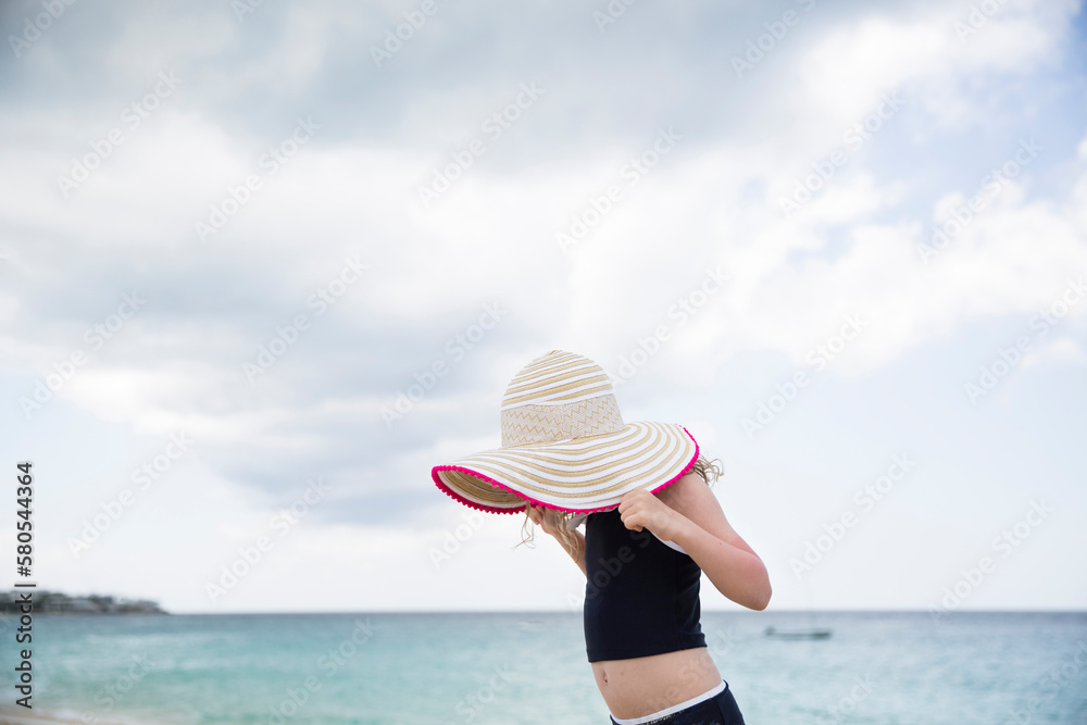 Side view of girl holding hat while standing against sea and cloudy sky at beach Side view of girl holding hat while standing against sea and cloudy sky at beach