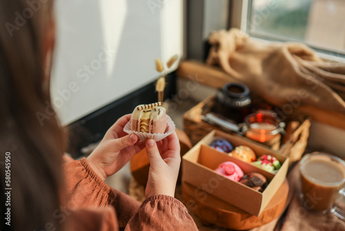Girl holding a macaron in her hand, with a box of assorted macarons in the background in a cozy home atmosphere