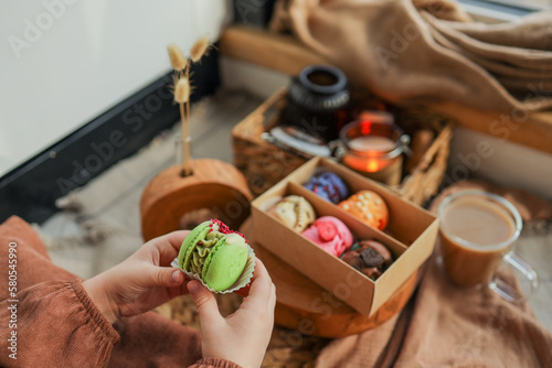Girl holding a macaron in her hand, with a box of assorted macarons in the background in a cozy home atmosphere