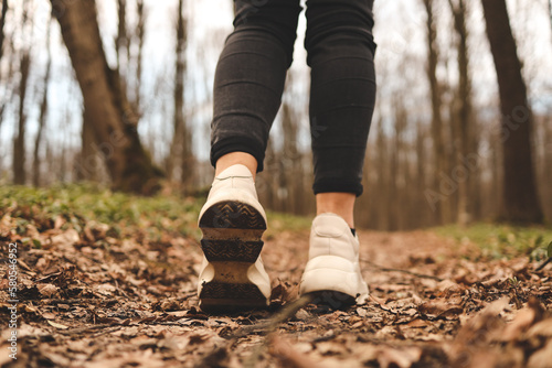 Close up of a womans legs running in the forest. Sport shoes. Trees and leaves in background. Active and healthy lifestyle concept
