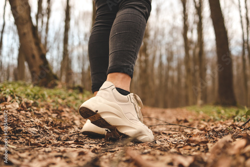 Close up of a womans legs running in the forest. Sport shoes. Trees and leaves in background. Active and healthy lifestyle concept