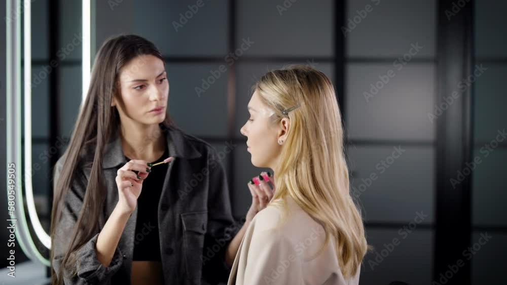 Make-up artist combs and styles the eyebrows of a young blonde woman in beauty salon