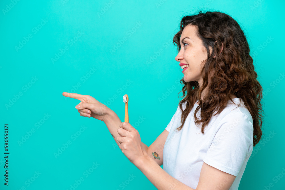 Young caucasian woman brushing teeth isolated on blue background pointing to the side to present a product Young caucasian woman brushing teeth isolated on blue background pointing to the side to present a product